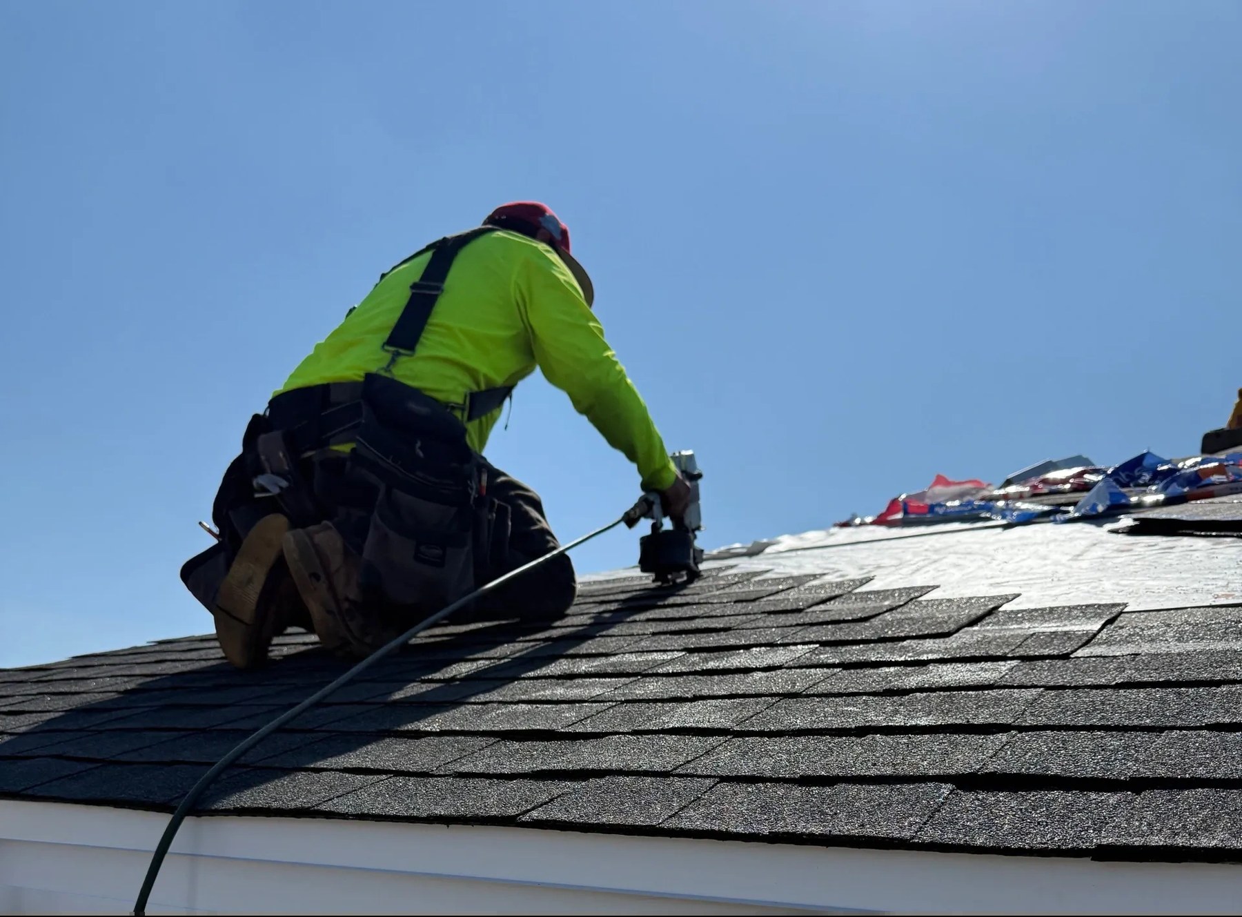 Roofer kneeling and fastening shingles on a sloped roof